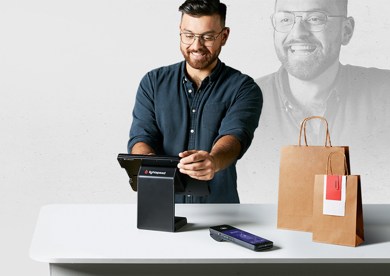 Un homme se tient derrière une caisse i-Pad avec deux sacs en papier à côté de lui.